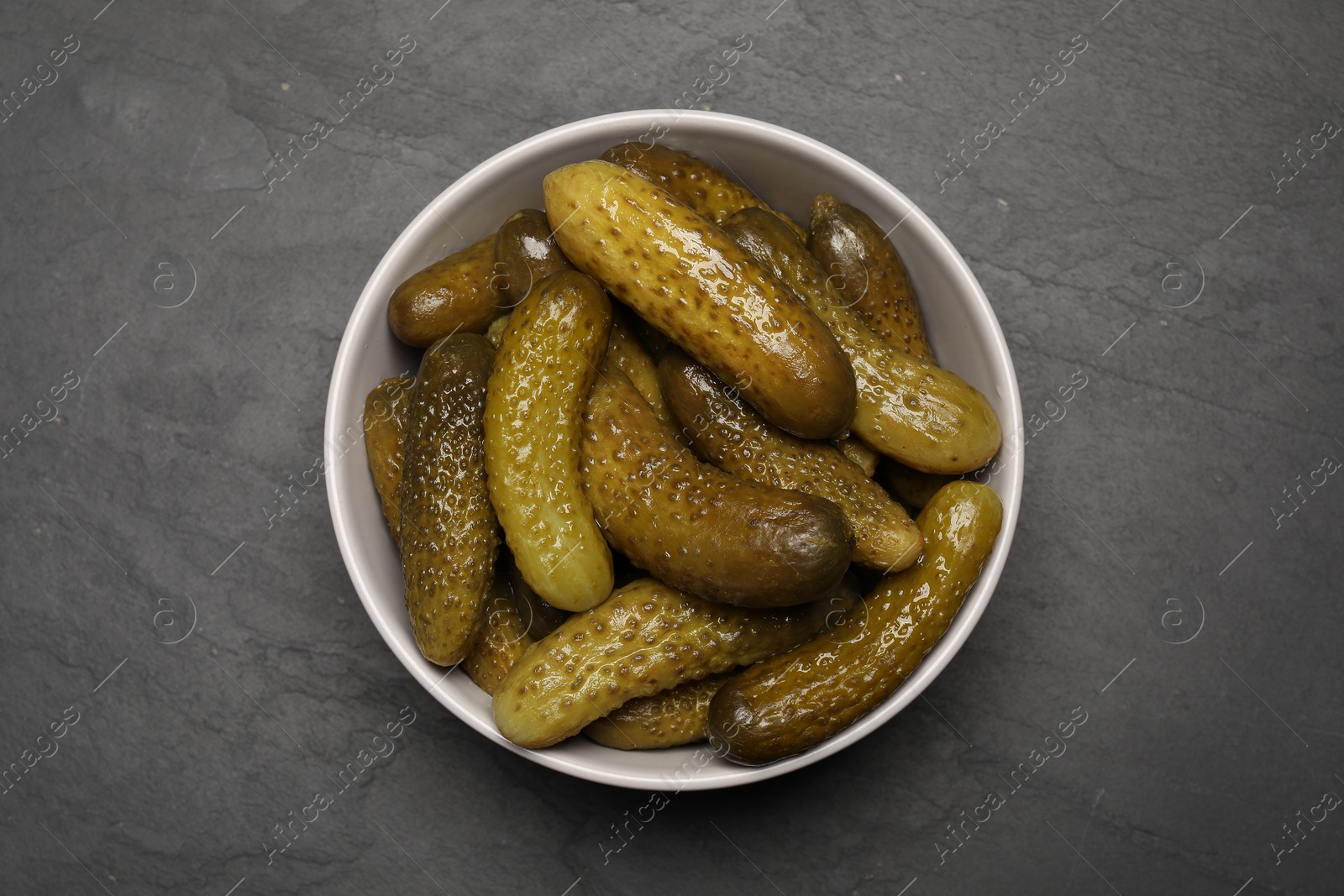 Photo of Tasty pickled cucumbers in bowl on grey textured table, top view