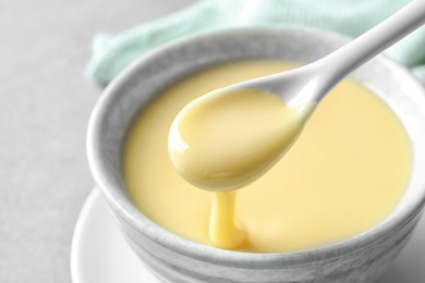 Spoon of pouring condensed milk over bowl on table, closeup. Dairy products