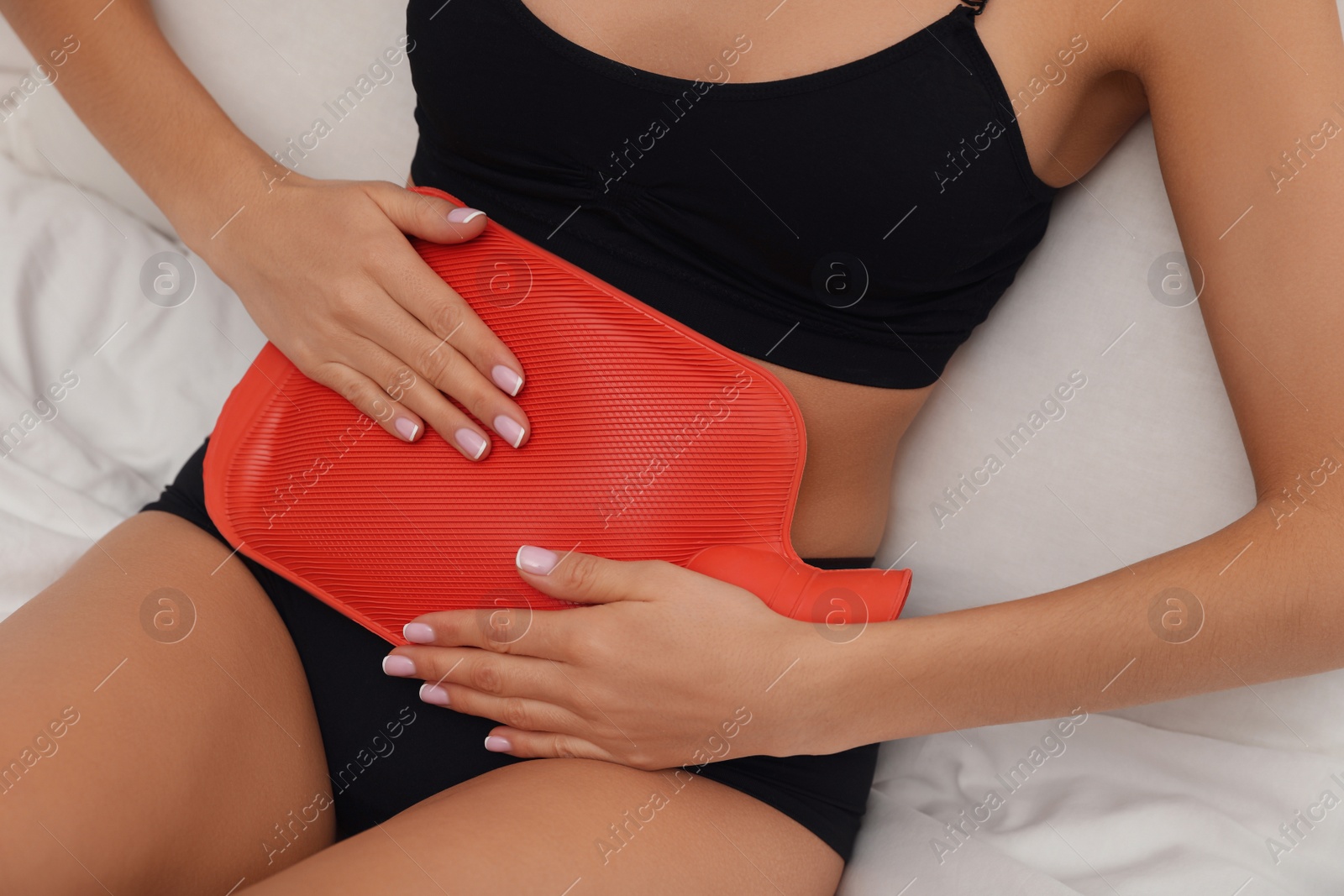 Photo of Woman using hot water bottle to relieve menstrual pain on bed at home, closeup