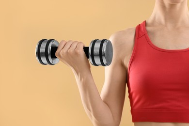Photo of Young woman in sportswear doing exercises with dumbbells on beige background, closeup. Space for text