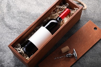 Bottle of wine in box, cork and corkscrew on dark textured table, above view