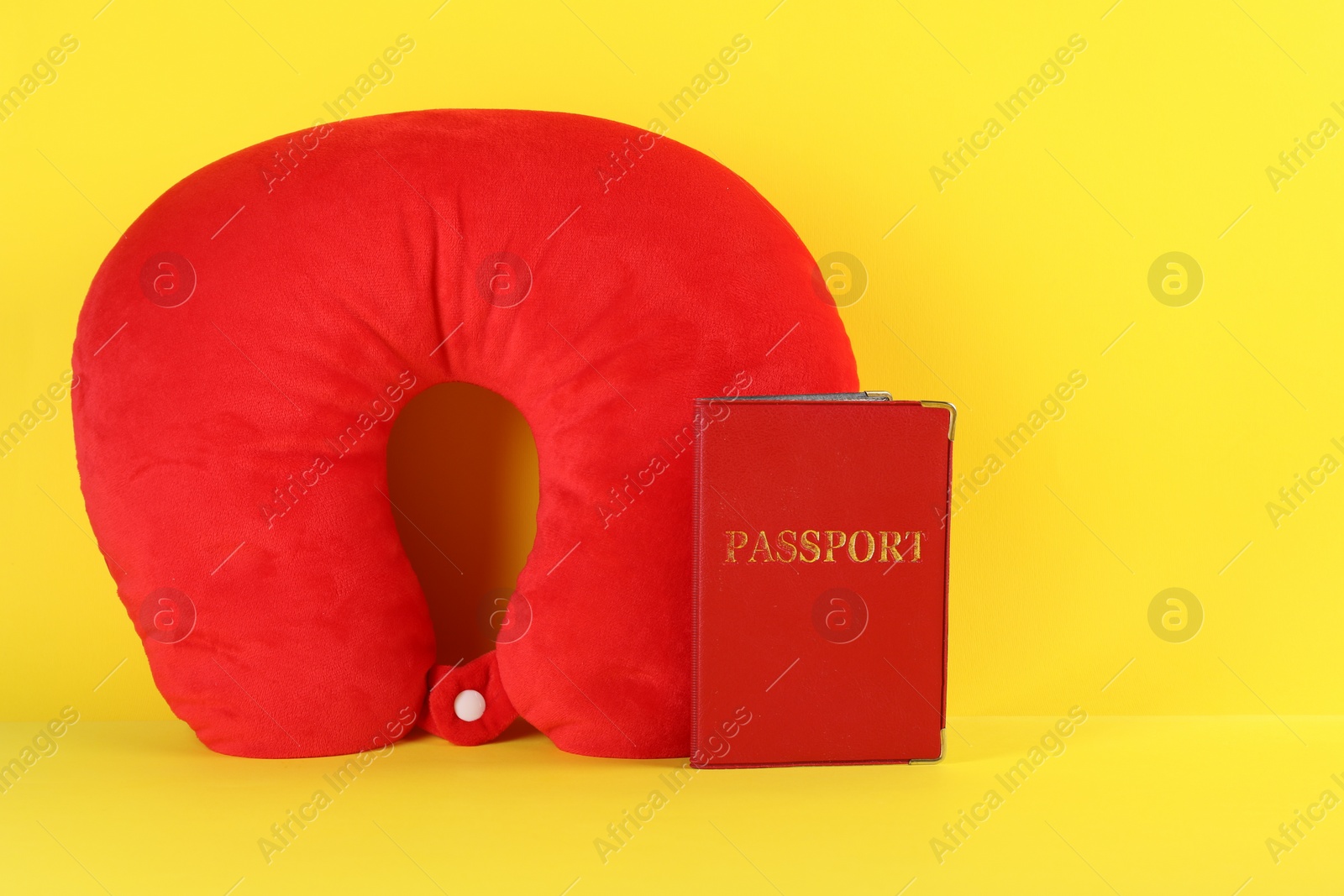 Photo of Red travel pillow and passport on yellow background