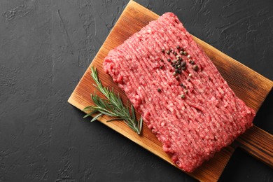 Photo of Raw ground meat, rosemary and peppercorns on black table, top view. Space for text