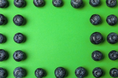 Frame of ripe blueberries on green background, flat lay with space for text