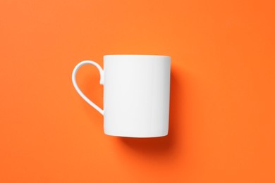 Photo of One white ceramic mug on orange background, top view
