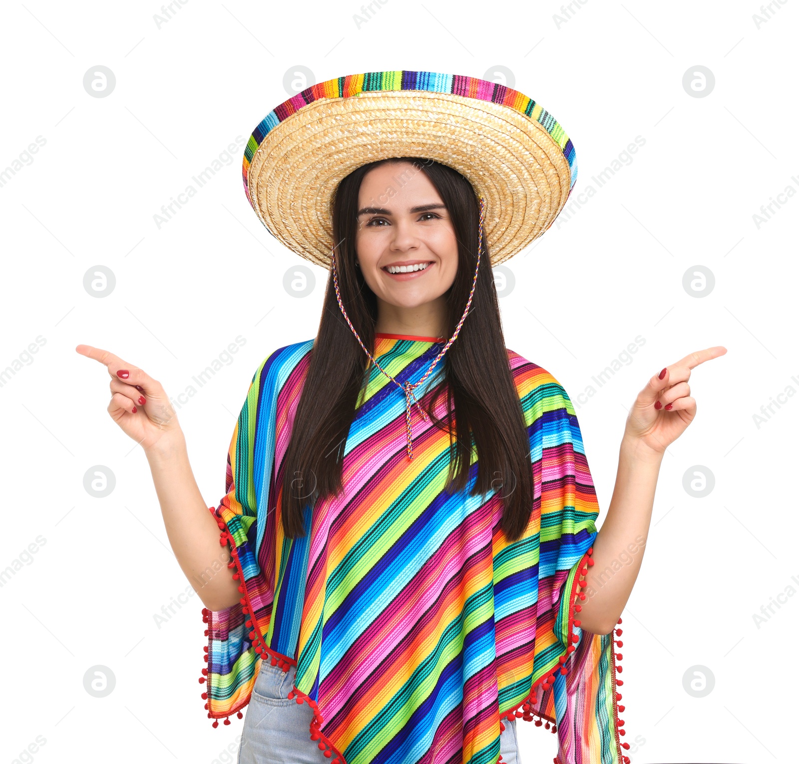 Photo of Young woman in Mexican sombrero hat and poncho pointing at something on white background