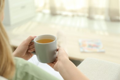 Photo of Young woman with cup of hot tea relaxing at home, closeup