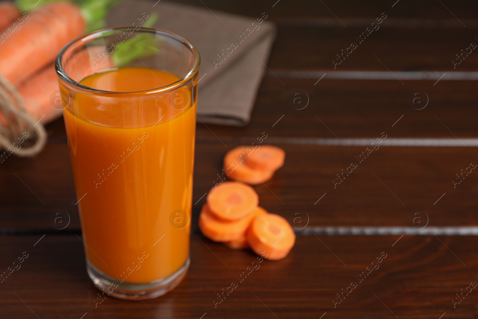 Photo of Glass of tasty carrot juice on wooden table, closeup. Space for text