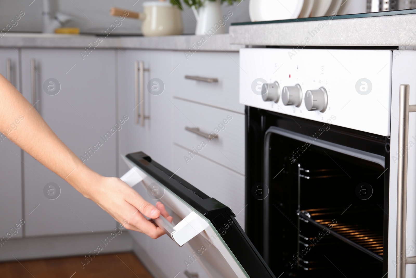 Photo of Woman opening electric oven in kitchen, closeup