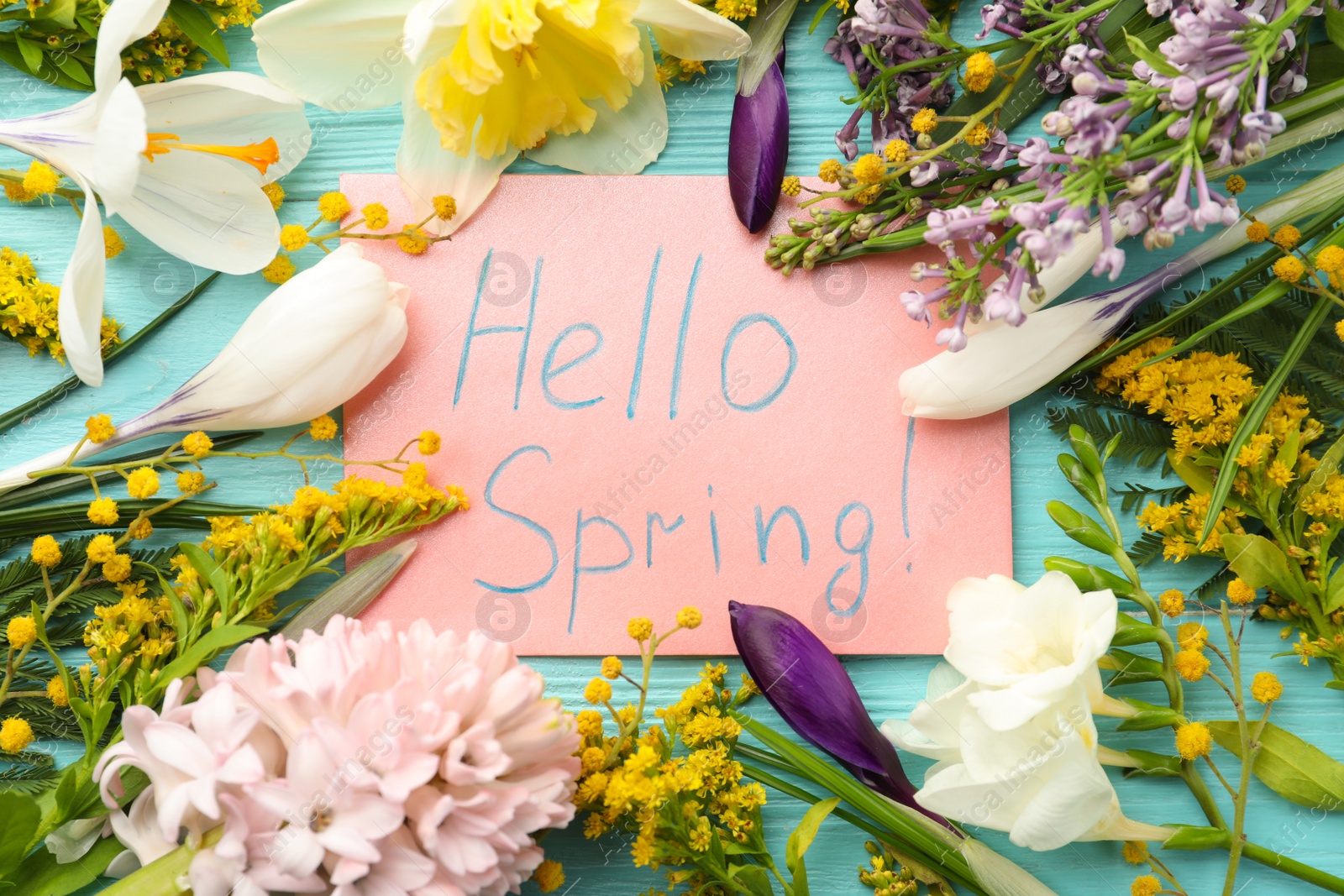 Photo of Pink card with words HELLO SPRING and fresh flowers on light blue wooden table, flat lay