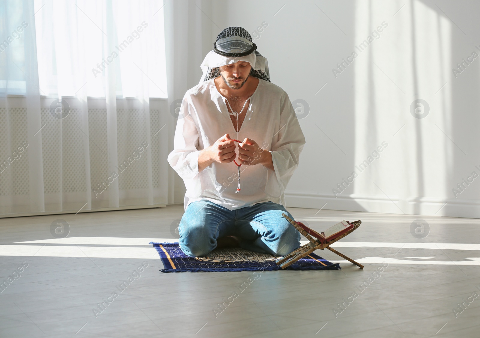 Photo of Muslim man in traditional clothes praying on rug indoors