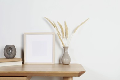 Photo of Empty photo frame and vase with dry decorative spikes on wooden table. Mockup for design