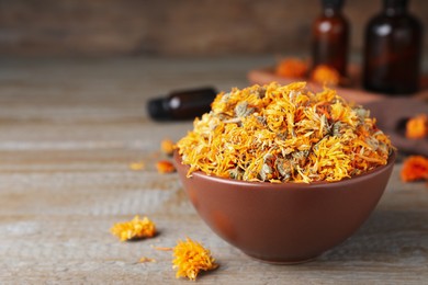 Photo of Bowl of dry calendula flowers on wooden table. Space for text