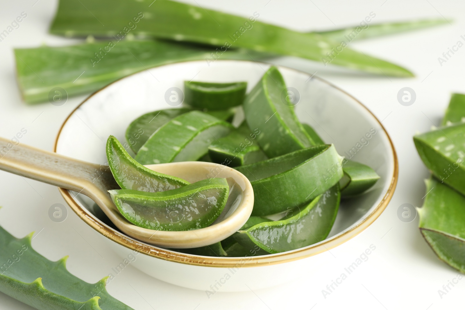 Photo of Bowl of fresh aloe vera pieces and spoon on white table