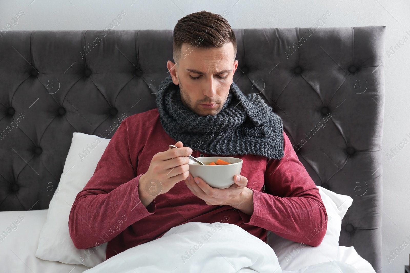 Photo of Sick young man eating broth to cure cold in bed at home