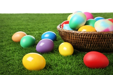 Photo of Wicker basket with bright painted Easter eggs on green grass