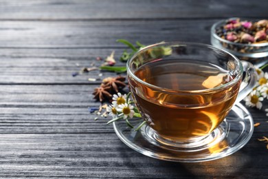 Glass cup of freshly brewed tea and chamomile flowers on black wooden table, closeup. Space for text