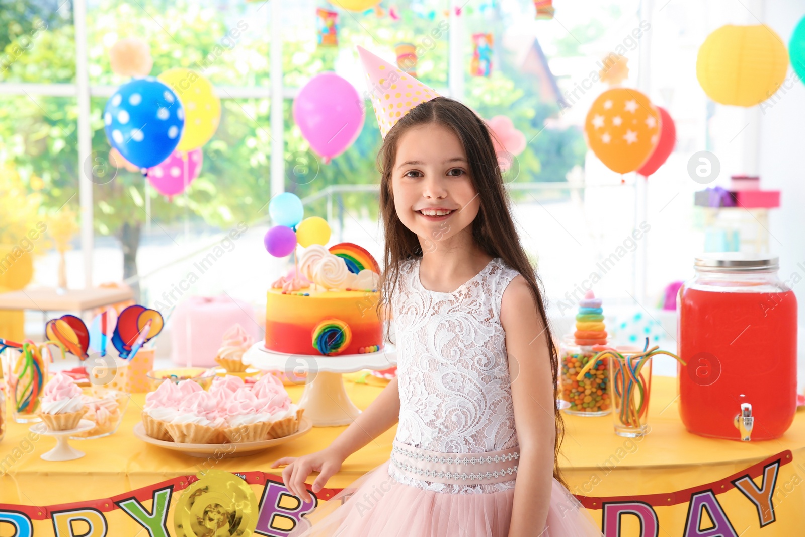 Photo of Cute little girl near table with treats at birthday party indoors