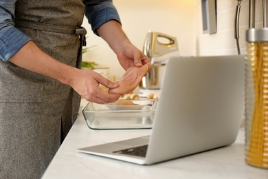 Photo of Man making dinner while watching online cooking course via laptop in kitchen, closeup