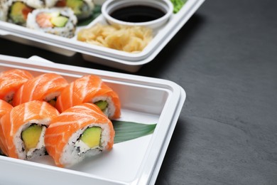 Photo of Food delivery. Delicious sushi rolls in plastic containers on black table, closeup with space for text