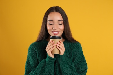 Photo of Happy beautiful woman with paper cup of mulled wine on yellow background