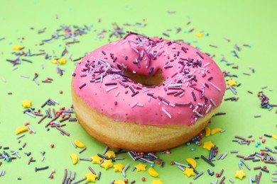 Photo of Glazed donut decorated with sprinkles on green background, closeup. Tasty confectionery