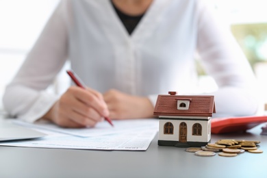 House model, coins and blurred woman on background. Tax day