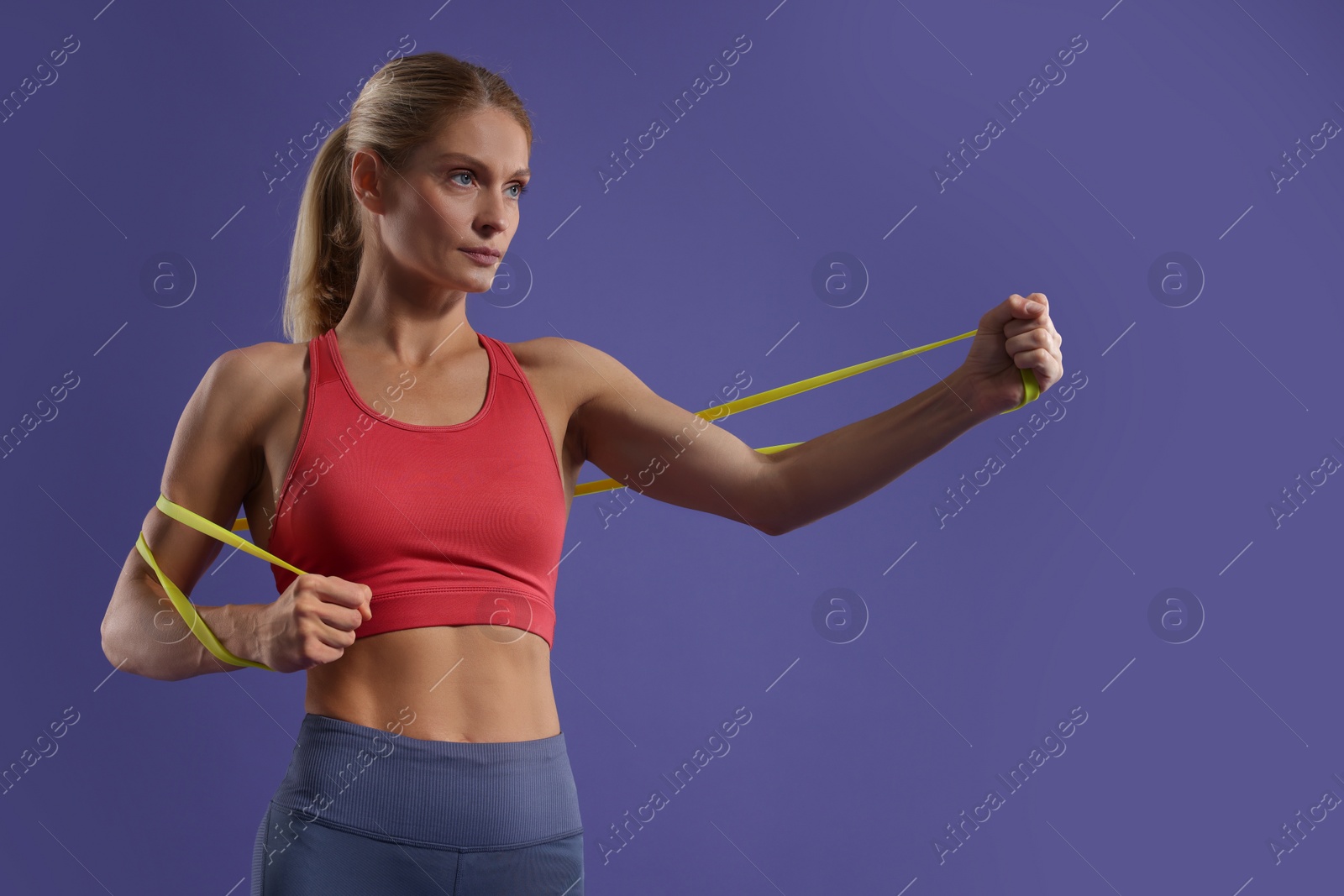 Photo of Athletic woman exercising with elastic resistance band on purple background