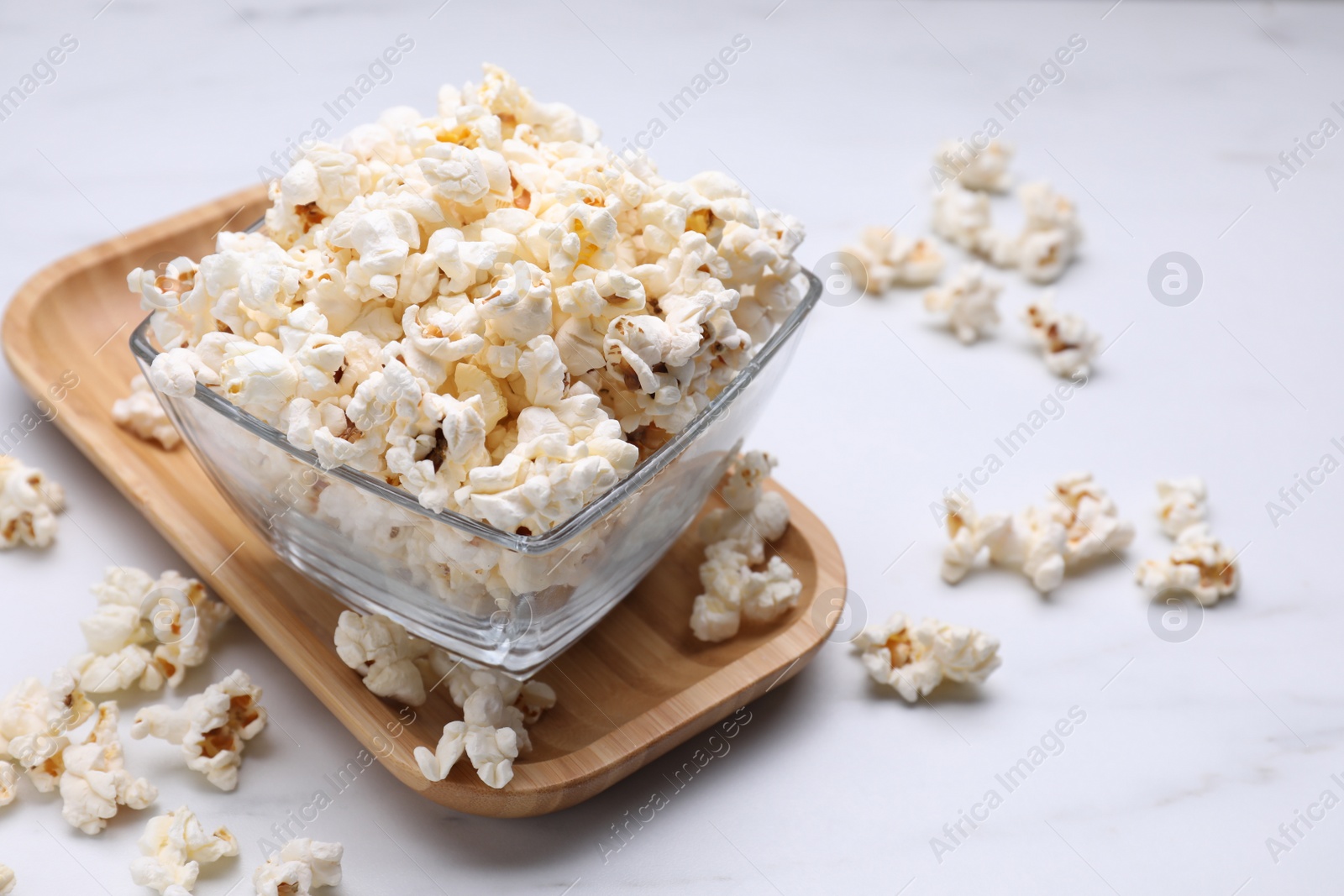 Photo of Bowl of tasty popcorn on white table, space for text