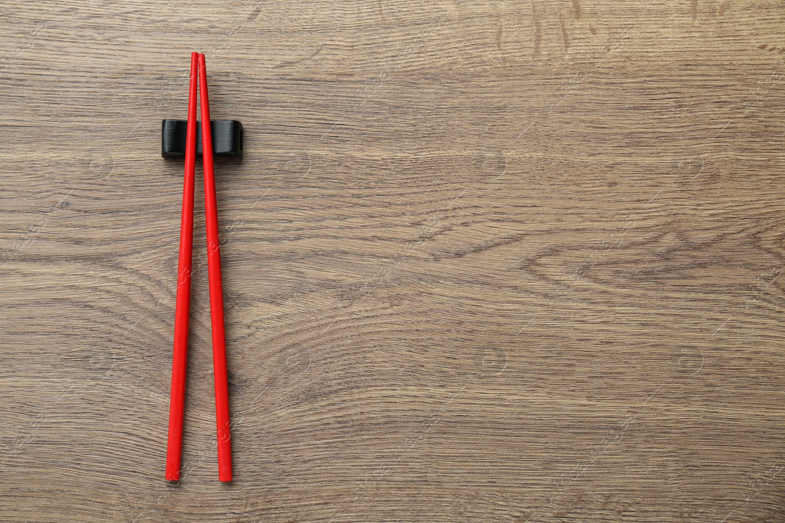 Photo of Pair of red chopsticks with rest on wooden table, top view. Space for text