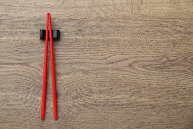 Pair of red chopsticks with rest on wooden table, top view. Space for text