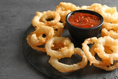 Photo of Delicious golden crispy onion rings and sauce on gray background, closeup