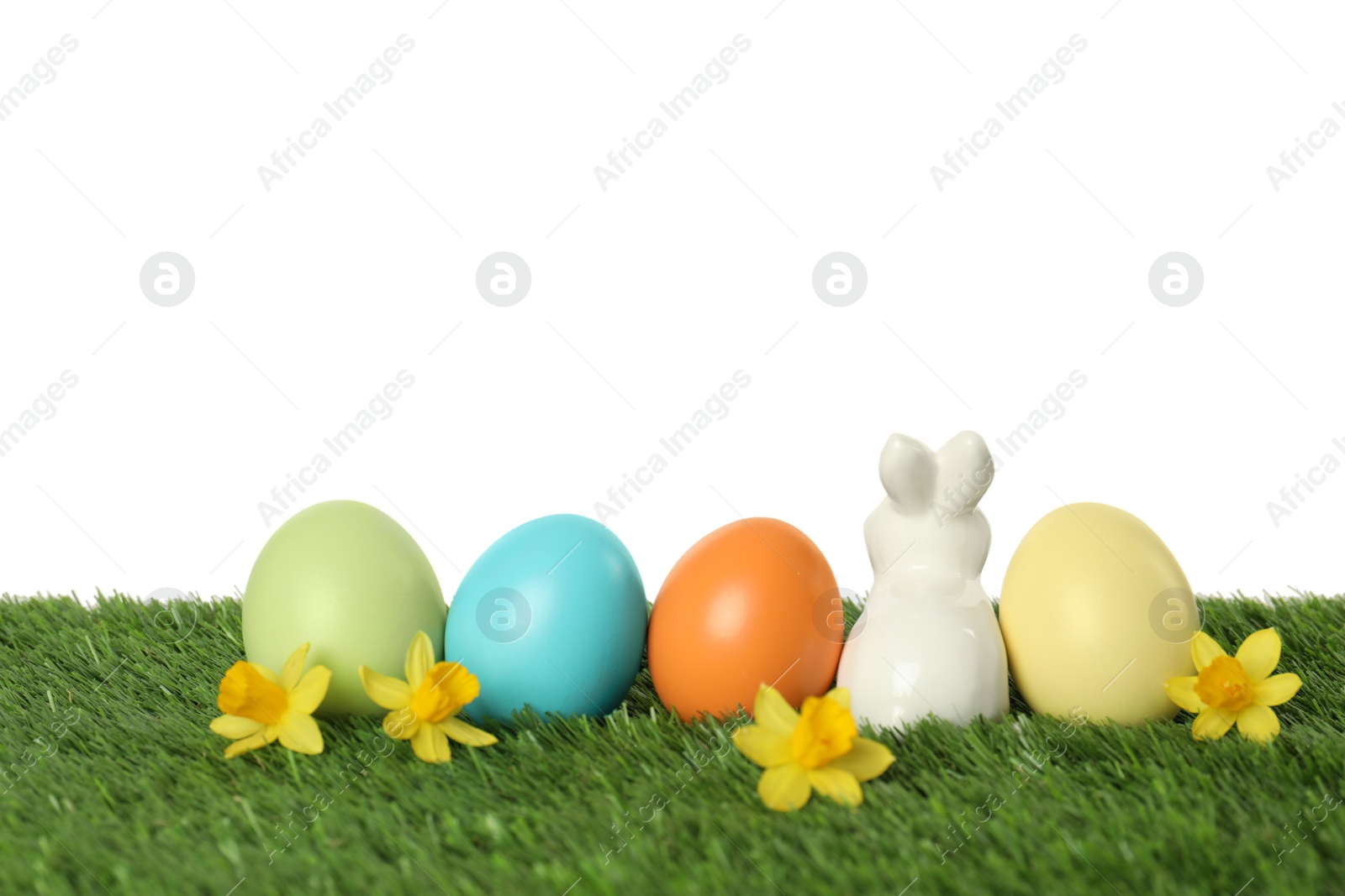 Photo of Ceramic Easter bunny and dyed eggs on green grass against white background