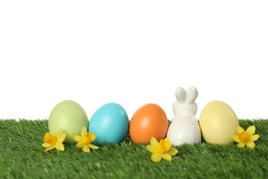 Ceramic Easter bunny and dyed eggs on green grass against white background