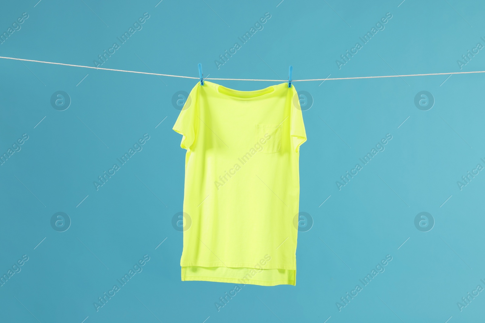 Photo of One green t-shirt drying on washing line against light blue background