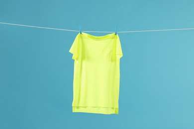 One green t-shirt drying on washing line against light blue background