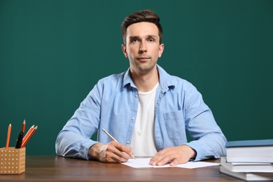 Portrait of male teacher working at table against color background