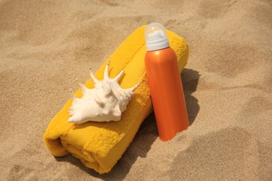 Photo of Sunscreen, seashell and rolled towel on sandy beach. Sun protection