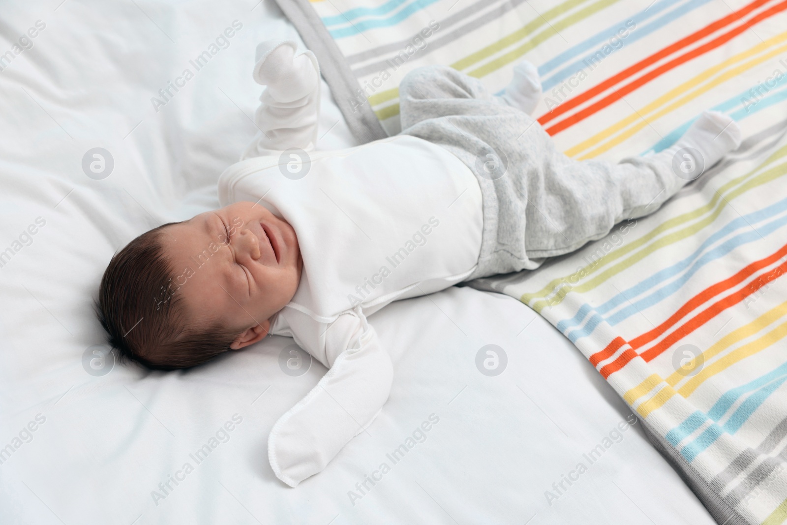 Photo of Cute newborn baby crying on soft bed
