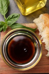 Bowl of organic balsamic vinegar with oil, basil and bread on grey table, flat lay