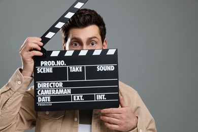 Actor holding clapperboard on grey background, space for text