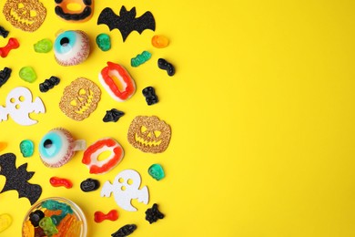 Photo of Tasty candies and Halloween decorations on yellow background, flat lay. Space for text