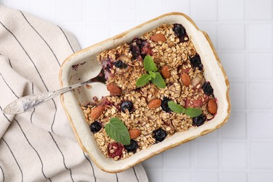 Photo of Tasty baked oatmeal with berries and almonds in baking tray on white tiled table, top view