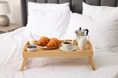 Photo of Wooden tray with tasty breakfast on bed at home