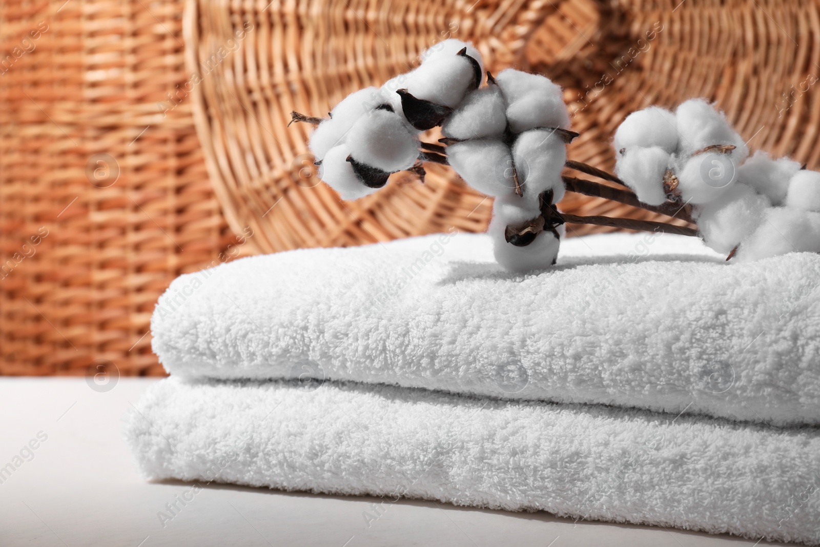 Photo of Stacked terry towels and cotton branches on white table, closeup. Space for text