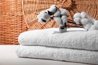 Stacked terry towels and cotton branches on white table, closeup. Space for text