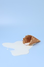 Melted ice cream and wafer cone on light blue background, space for text