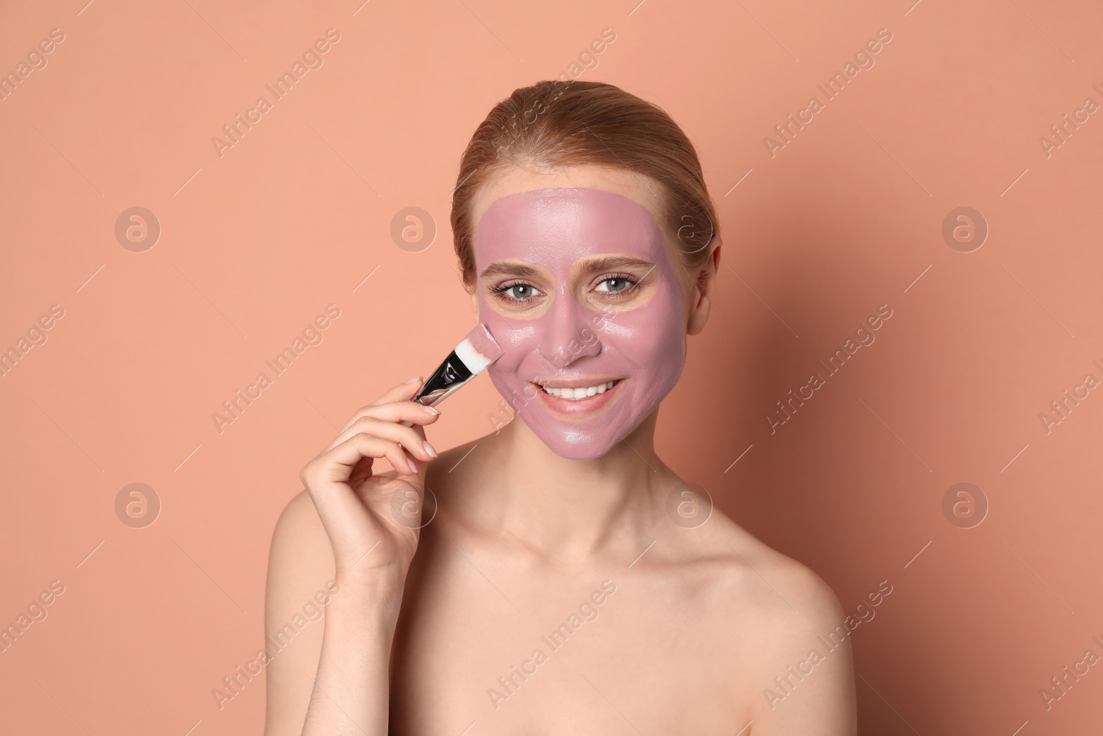 Photo of Young woman applying pomegranate face mask on pale coral background