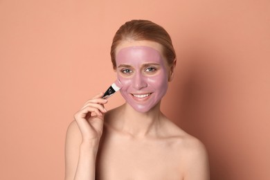 Photo of Young woman applying pomegranate face mask on pale coral background