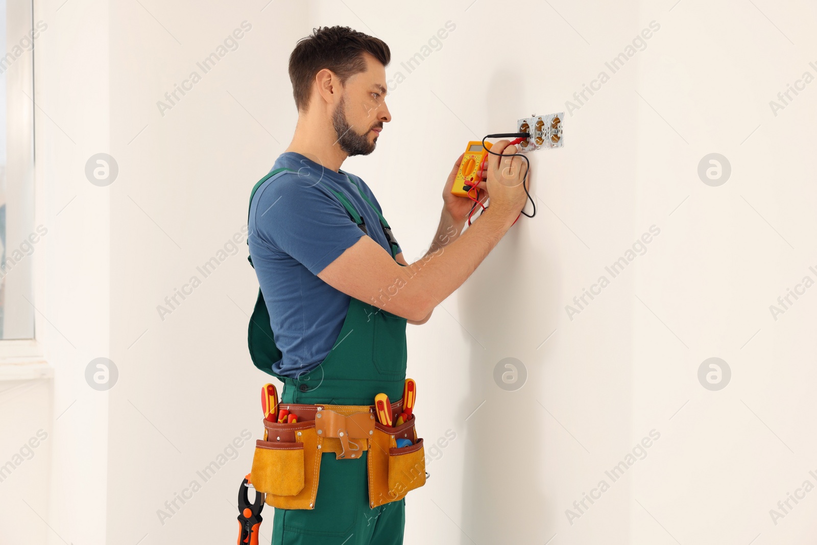 Photo of Electrician in uniform with tester checking voltage indoors